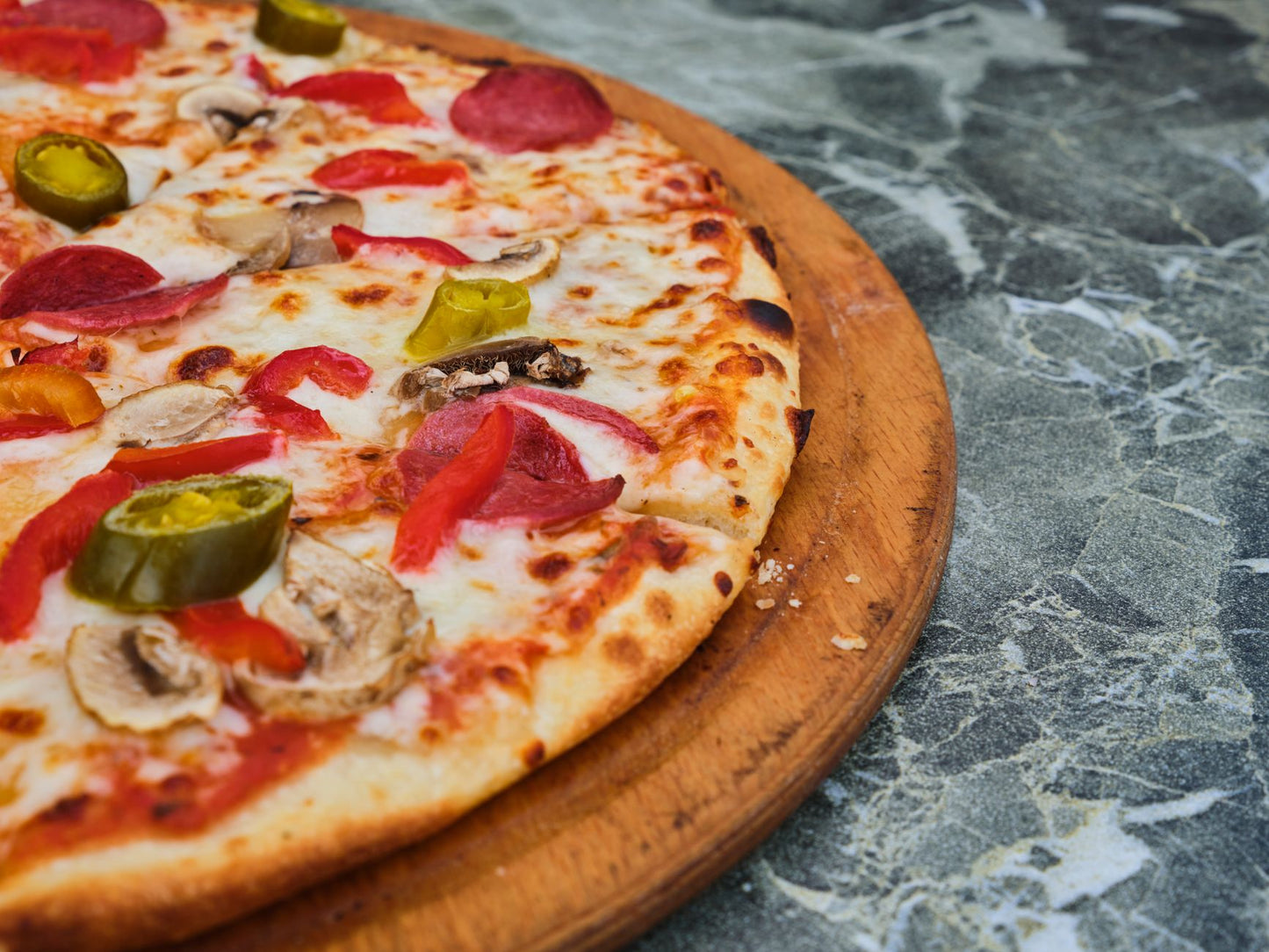 Freshly baked pepperoni pizza slice topped with jalapenos and mushrooms on a wooden tray.