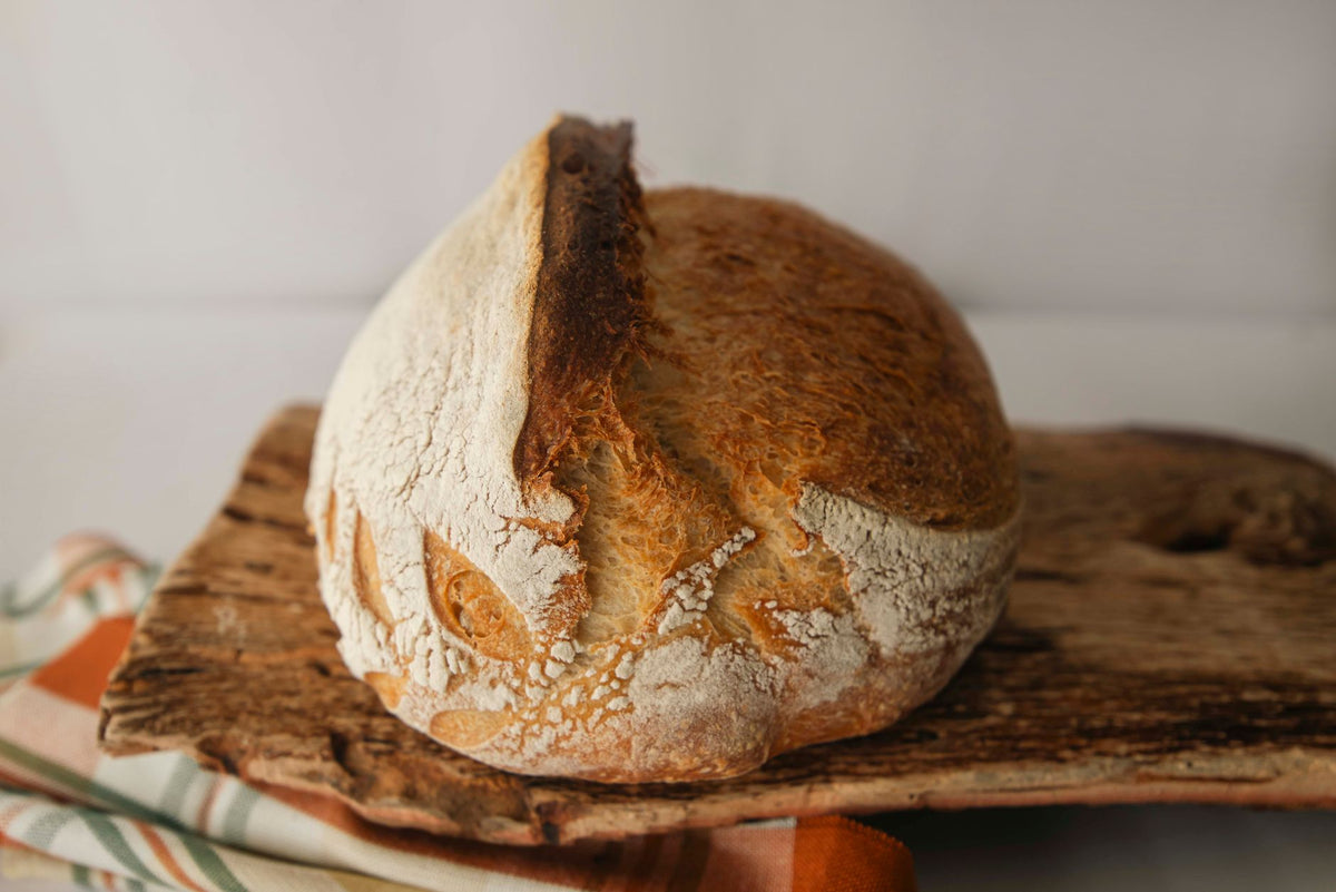 Freshly baked artisan sourdough loaf on a rustic wooden board, perfect for bakery themes.