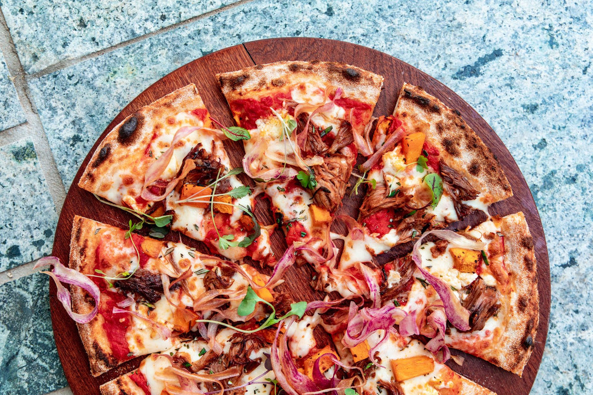 Top view of a sliced gourmet pizza with vegetables on a wooden board, perfect for food photography.