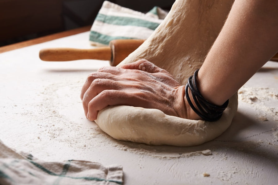 Hands stretching a floured pizza dough ball on a work surface, the dough-handling half of the Pizza Pro Pack