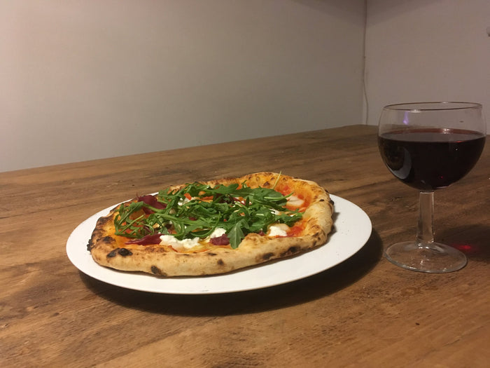Rocket-topped pizza beside a glass of red wine