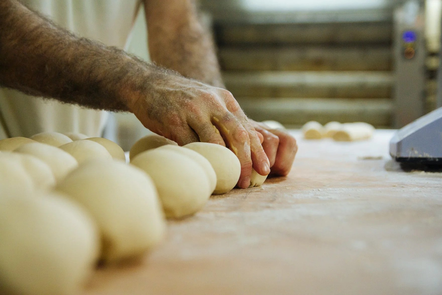 A baker shaping rows of dough balls on a floured bench