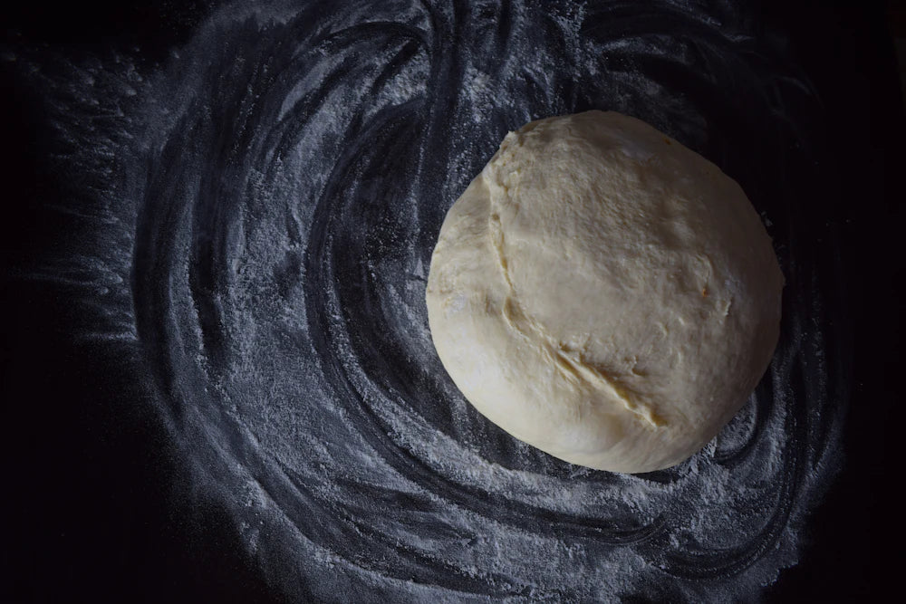 A round of bread dough resting on a dark, floured surface