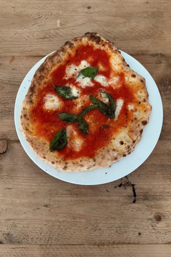 A home-baked Neapolitan margherita with a puffed, leopard-spotted cornicione on a white plate